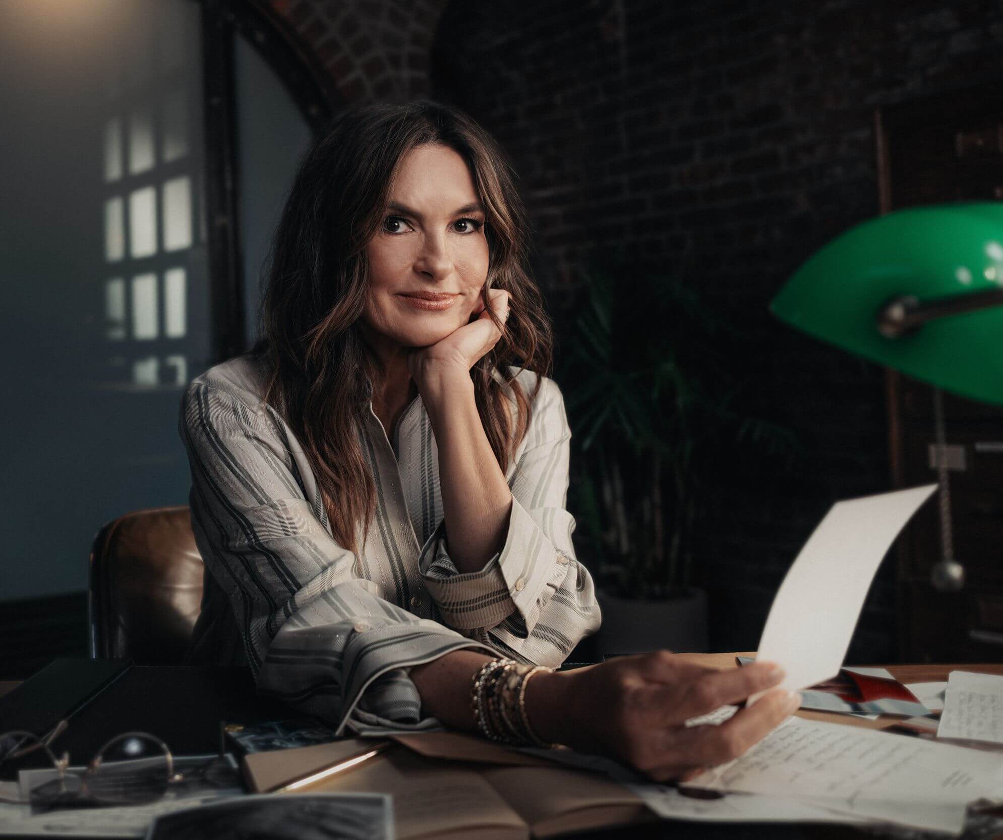 Mariska Hargitay sitting at a desk, holding a notecard and deep in thought.